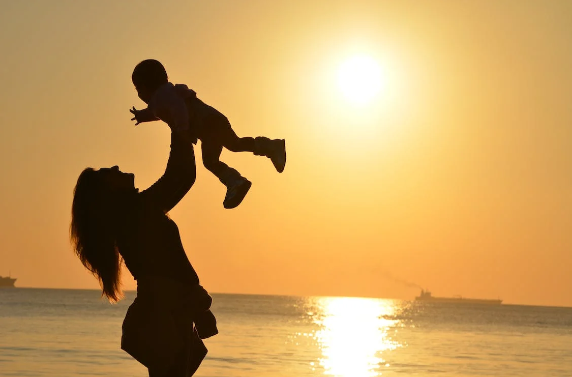 a woman throws and catches her son against the background of the sea