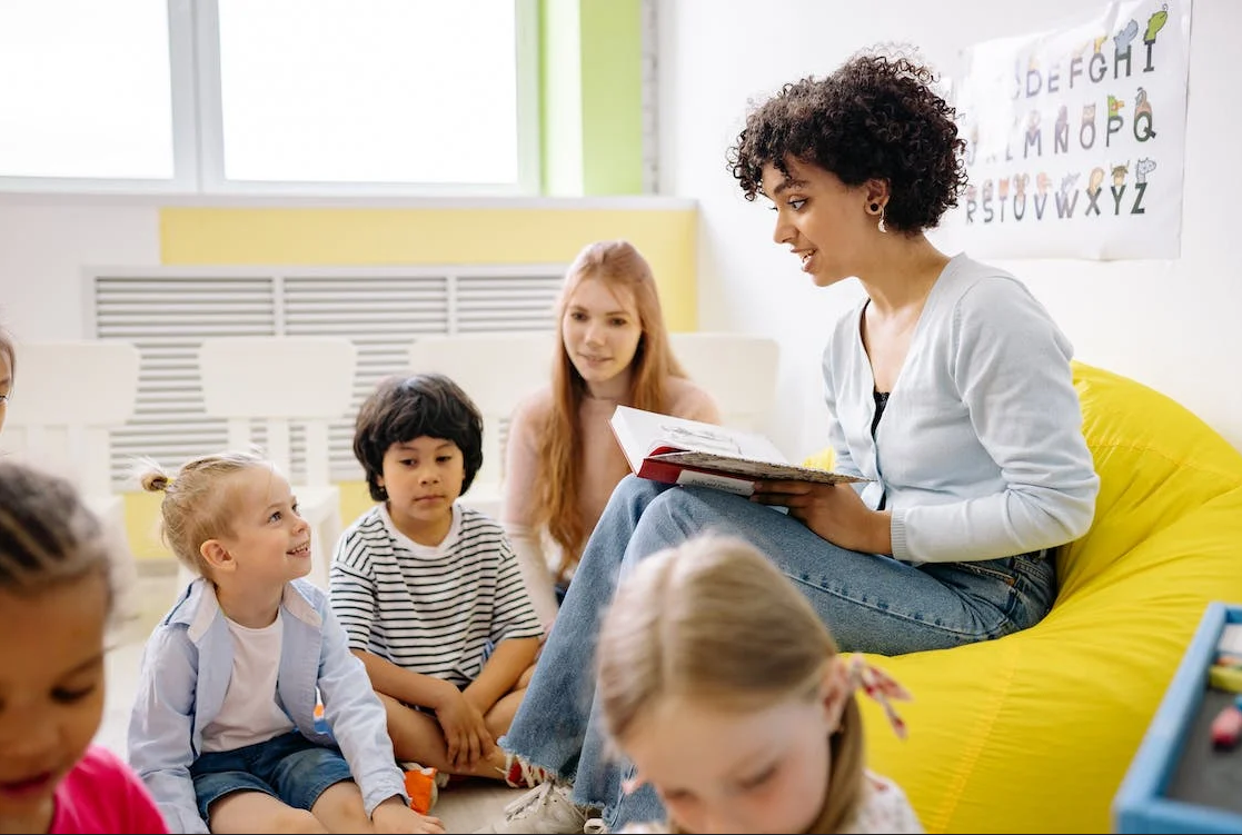 a woman teaches children holding a book in her hands sitting on a yellow chair